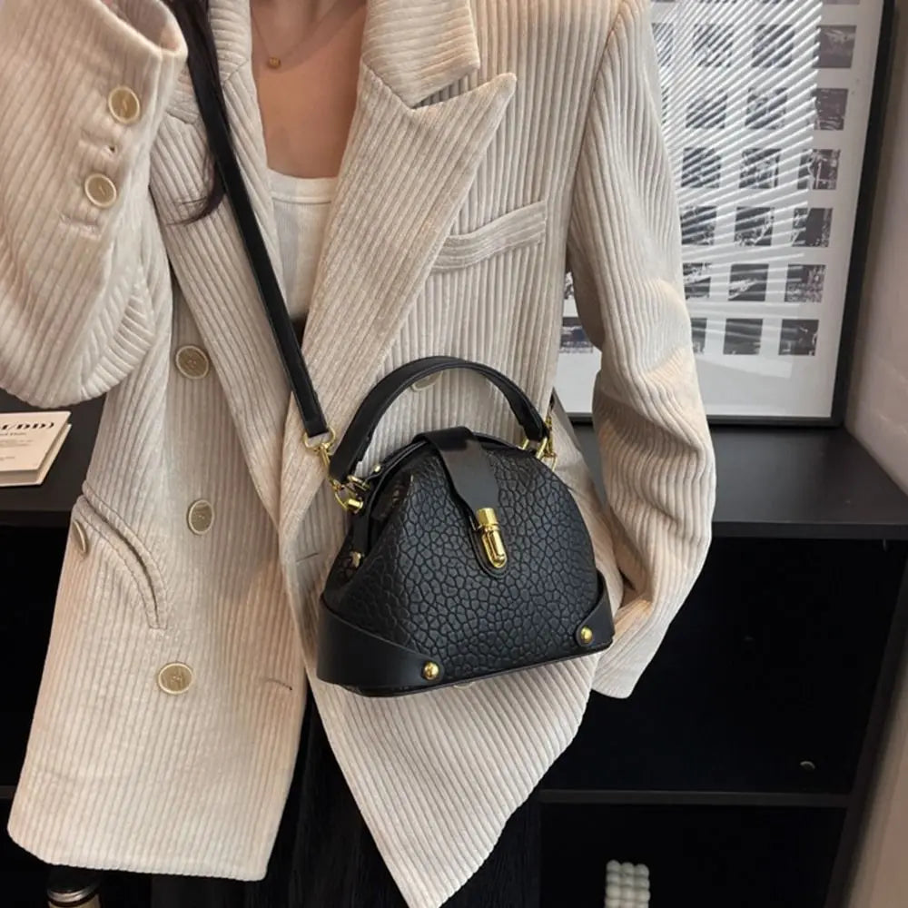 Woman wearing a cream blazer and carrying a black textured dome satchel bag.