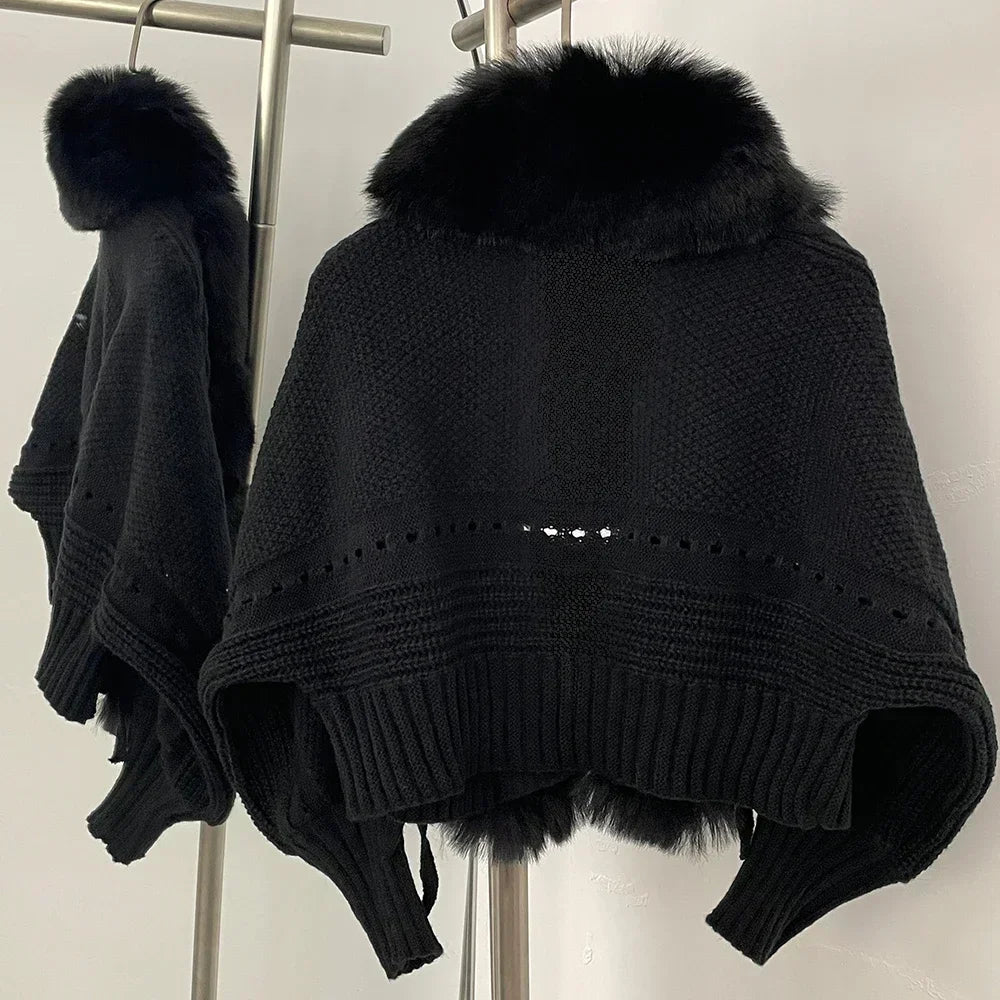 Black knitted poncho with fur trim on a stand against a neutral background