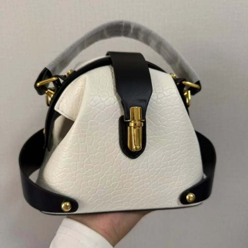 Textured dome satchel bag with black contrast trim and gold buckle closure, held in hand.