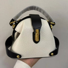 Textured dome satchel bag with black contrast trim and gold buckle closure, held in hand.