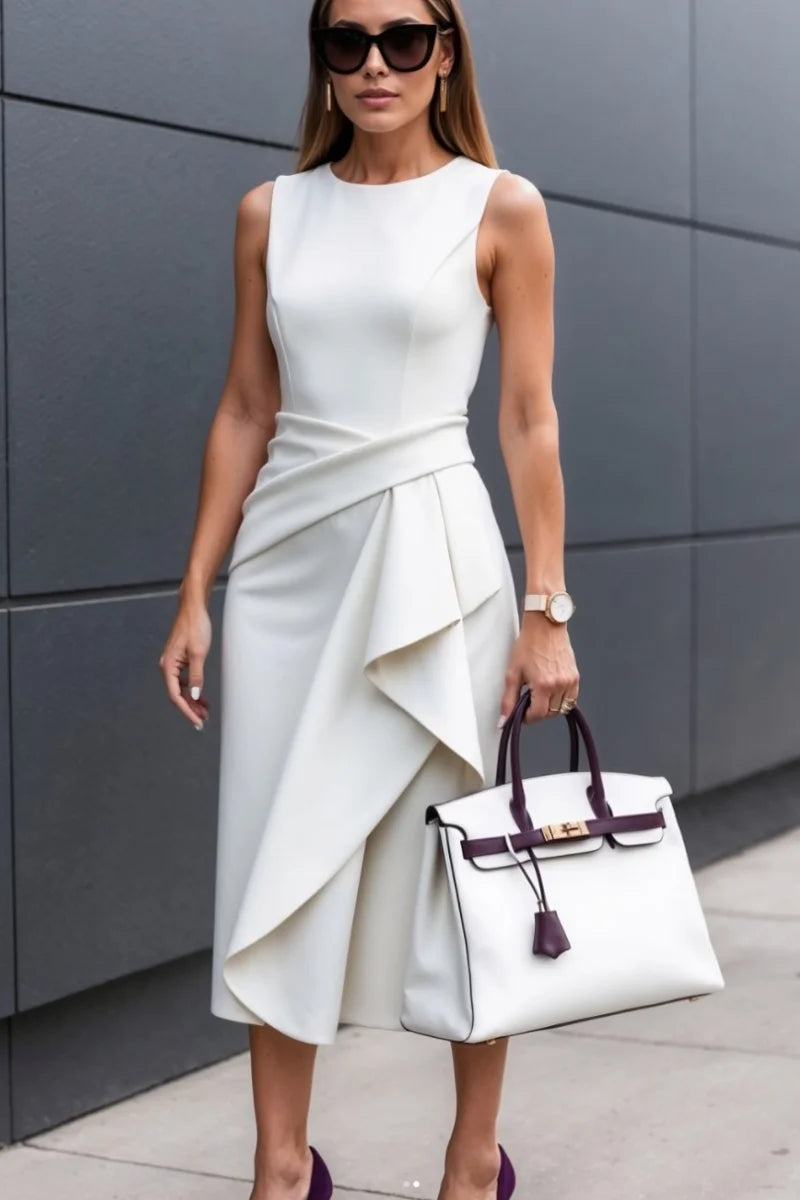 Woman in a white dress holding a white handbag against a gray wall.