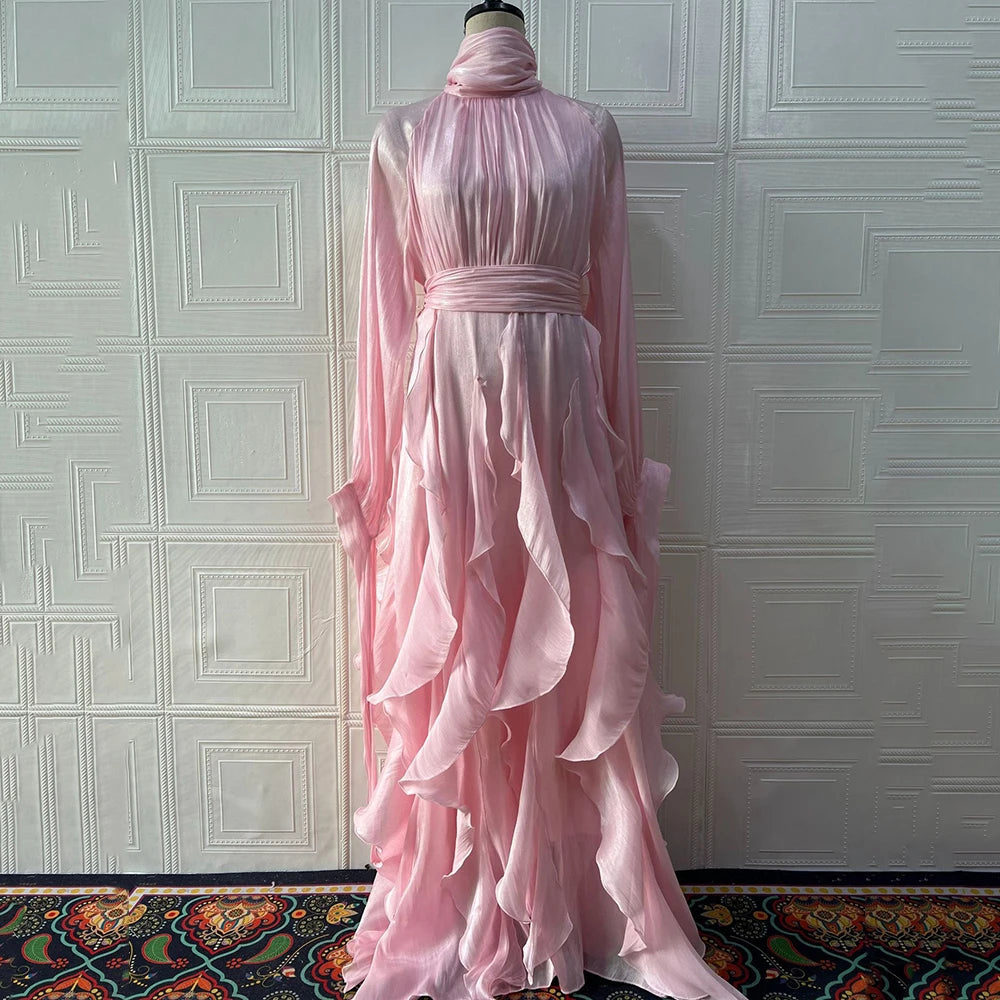 Pink ruffled dress on a mannequin against a textured white wall.
