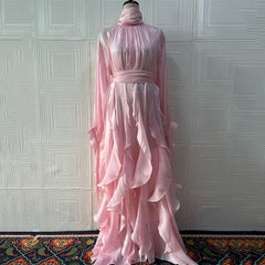 Pink ruffled dress on a mannequin against a textured white wall.