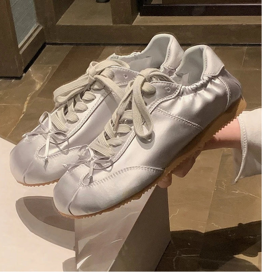 Silver grey satin ballet sneakers held by hand.