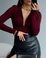 Person wearing a burgundy long-sleeve top and black leather skirt, holding a phone.