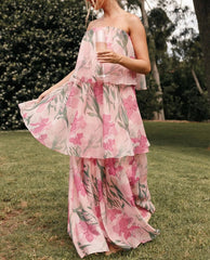 Woman wearing a pink floral dress standing outdoors on grass with trees in the background
