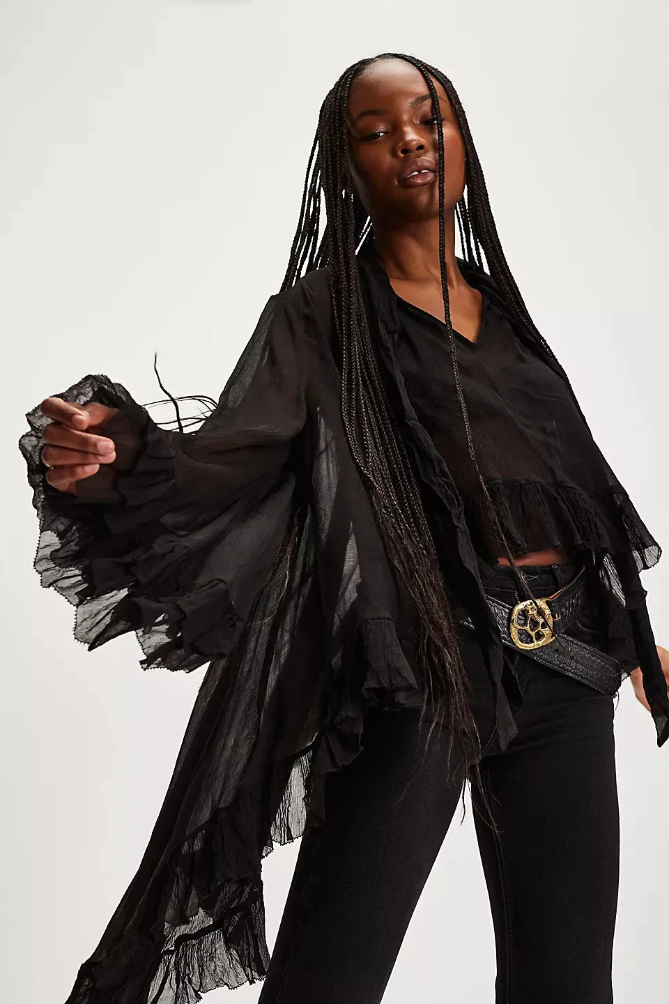 Woman wearing a black outfit with ruffled sleeves and a belt on a white background