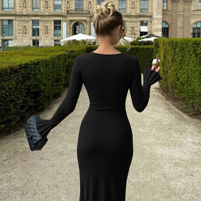 Woman in a black dress walking outdoors with a building and greenery in the background