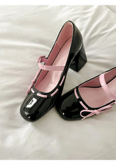 Close-up of black patent leather chunky Mary Jane heels on a white surface.