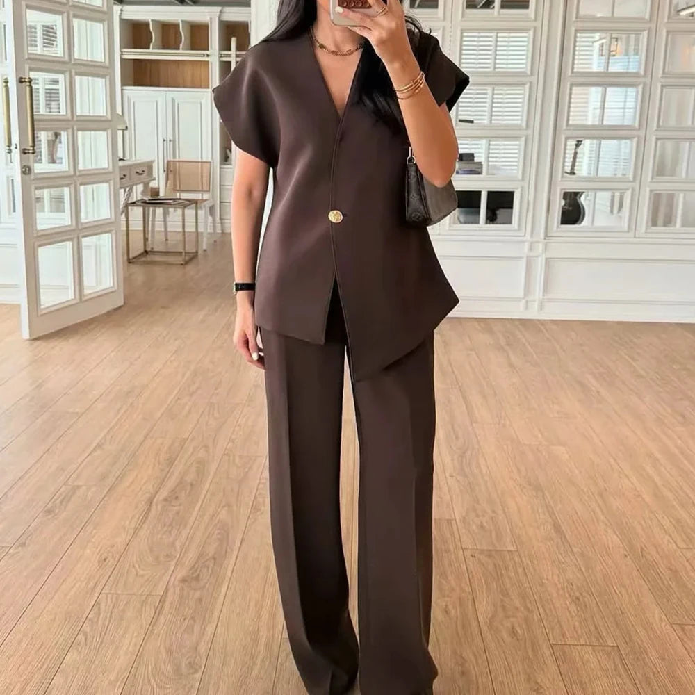 Person wearing a brown outfit with a gold button in a room with wooden flooring and white walls.