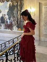 A woman posing in a flowing red dress with layered ruffles, accentuating the elegant silhouette.