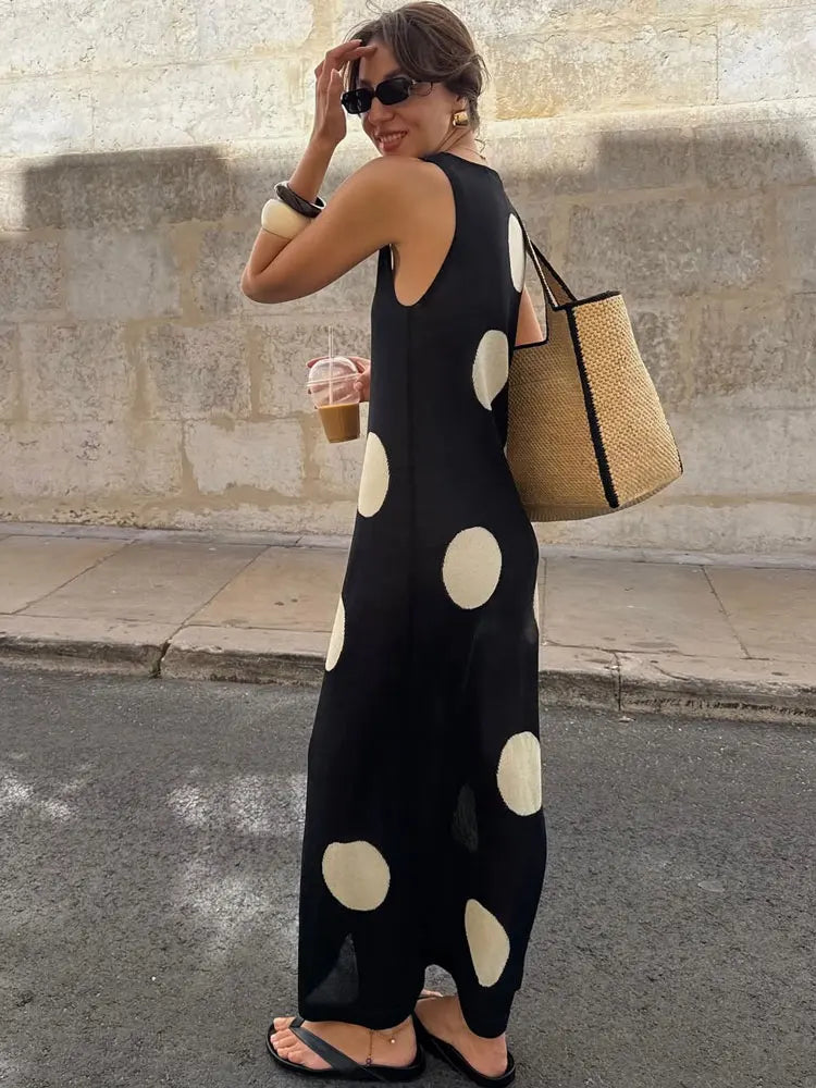 Woman in a black polka dot dress holding a beige bag on a street.