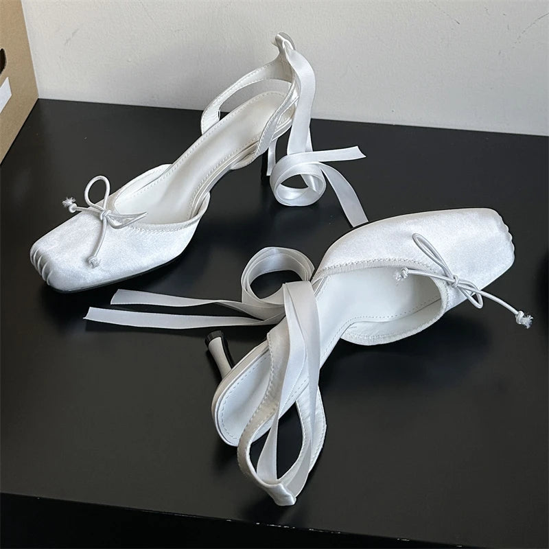White high-heeled shoes with ribbon details on a black surface