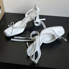 White high-heeled shoes with ribbon details on a black surface
