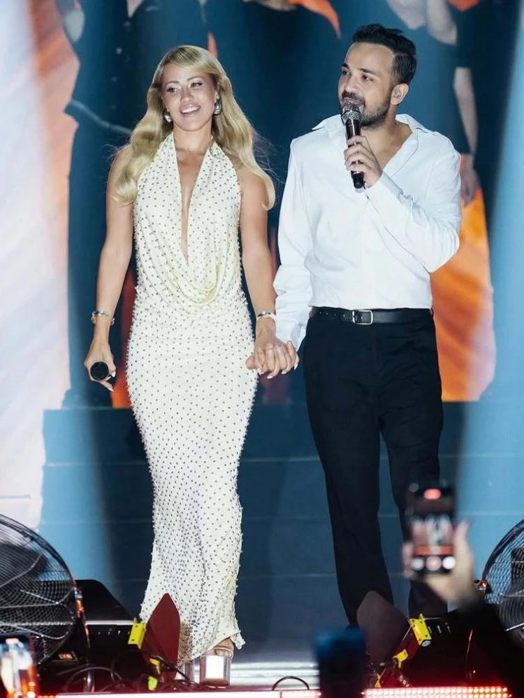 Two people on stage, one in a long white dress and the other in a white shirt and black pants, with a microphone.