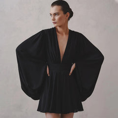 Woman wearing a black dress with wide sleeves against a plain background