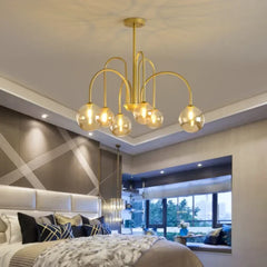 Gold chandelier hanging in a modern bedroom with a bed and large window.