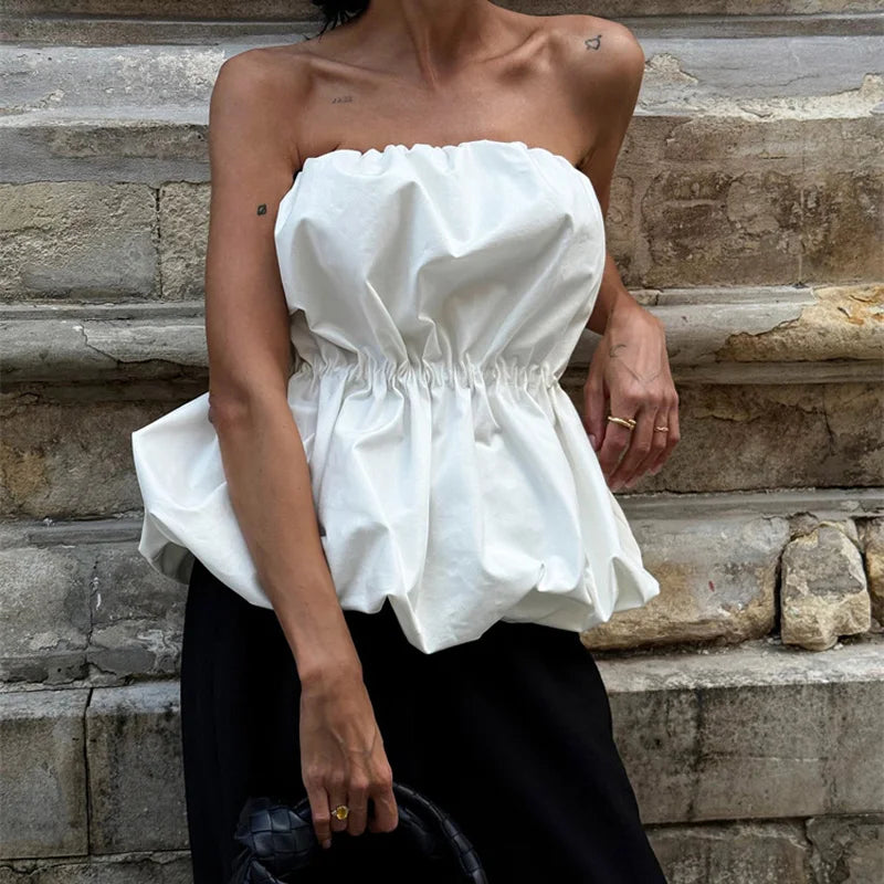 Person wearing a white strapless top sitting on stone steps.