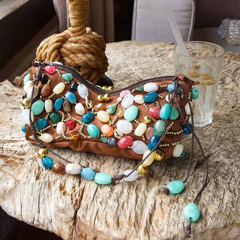Brown beaded stone shoulder bag on a rustic wooden surface next to a drink.