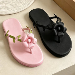 Pair of pink and black satin flip flops with floral embellishments.