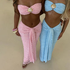 Two women wearing pink and blue sarongs with shell details on a beige background