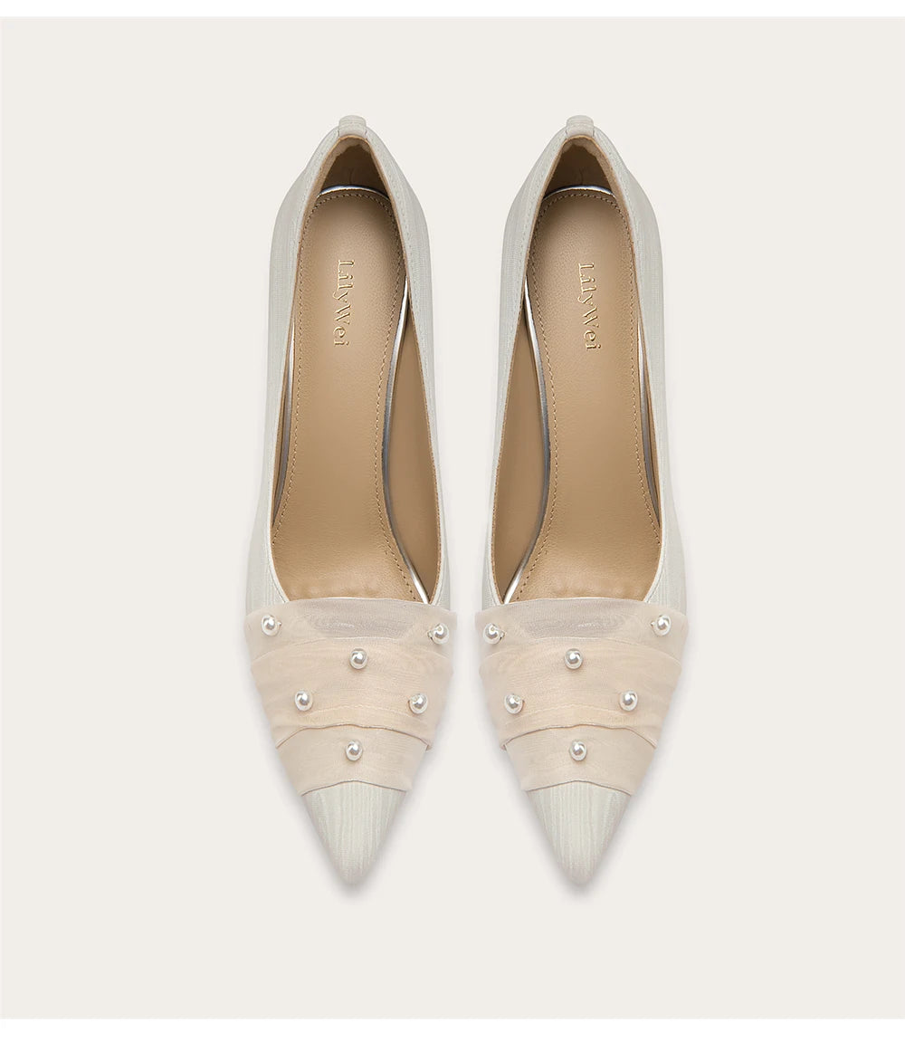 Pair of beige high-heeled shoes with pearl embellishments on a white background