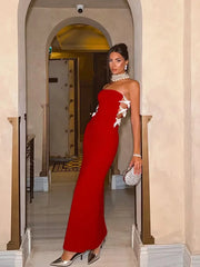 Woman in a red strapless dress with white floral details standing in an elegant interior setting.
