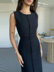 Woman wearing a black sleeveless dress with buttons in an indoor setting.