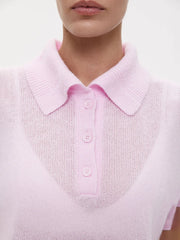 Close-up of a person wearing a light pink knitted polo shirt with a plain background
