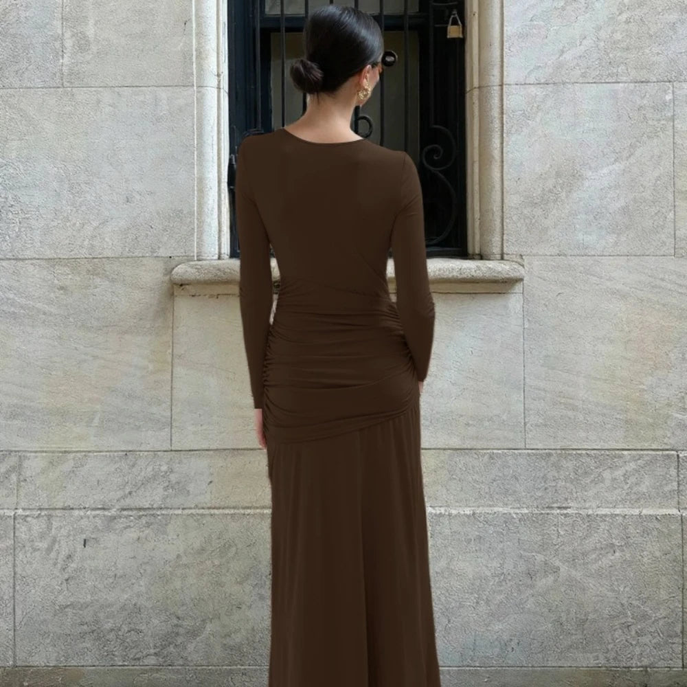 Woman in a brown dress standing against a stone wall.