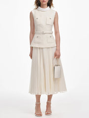 Woman wearing a cream-colored sleeveless top and pleated skirt with a white handbag on a white background