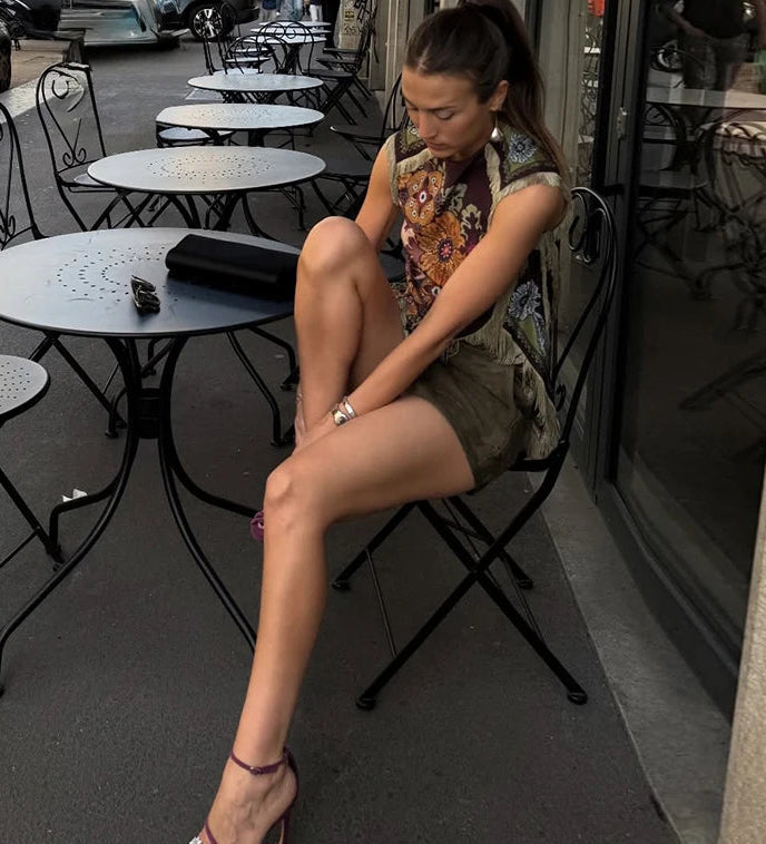 Woman sitting on a chair outside a cafe with tables and chairs around her.
