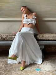 Woman in a white outfit with floral details sitting on a bench.