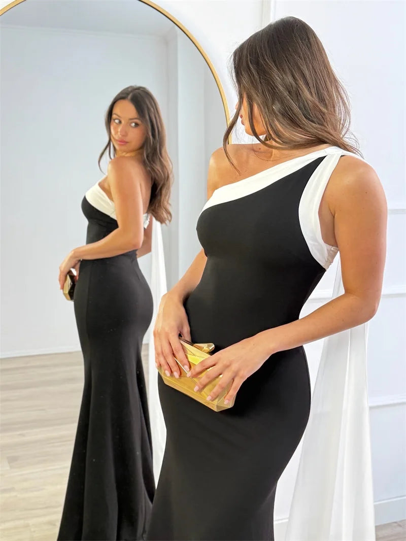 Woman in a black and white dress holding a gold clutch in front of a mirror.