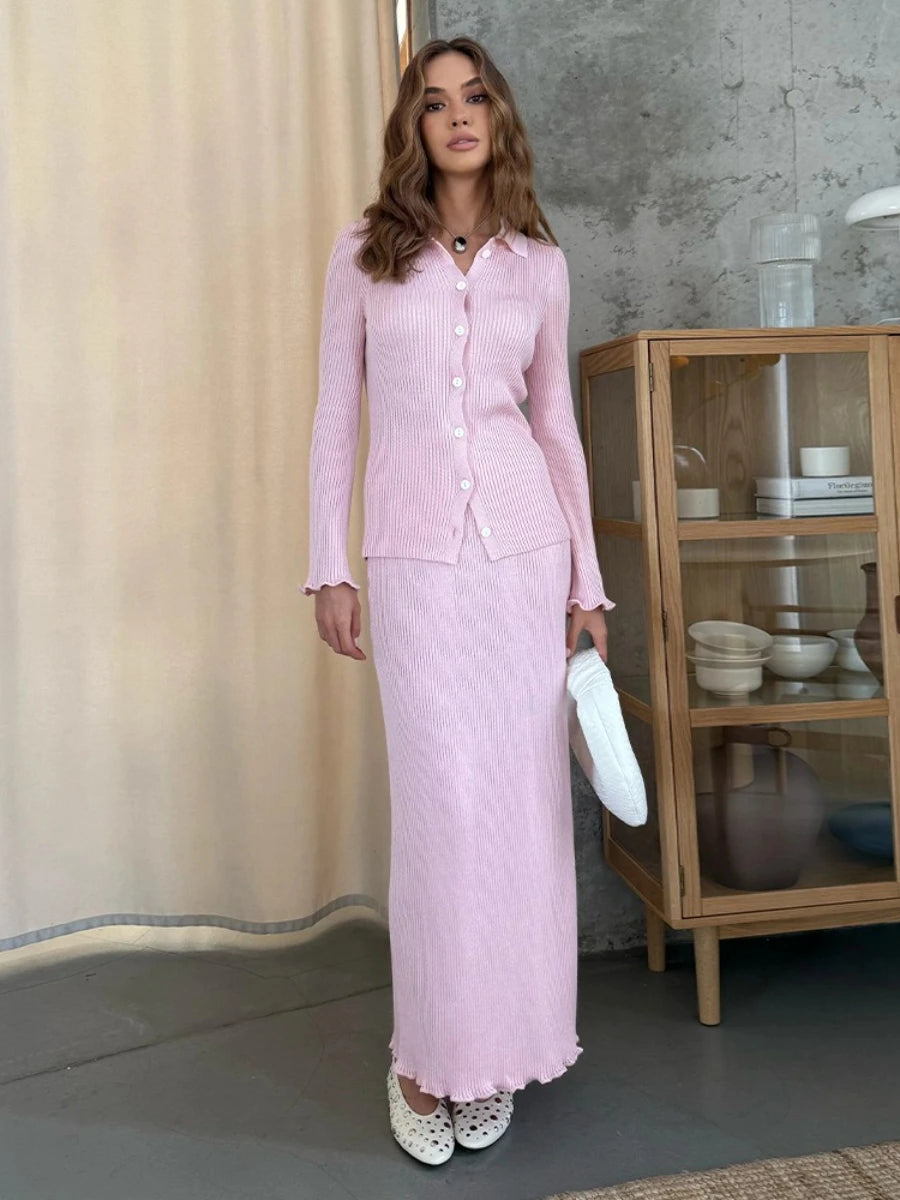 Woman in a pink outfit standing in a room with a curtain and wooden cabinet.