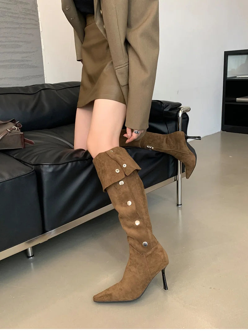 Brown suede knee-high boots with button details worn by a person sitting on a black sofa.