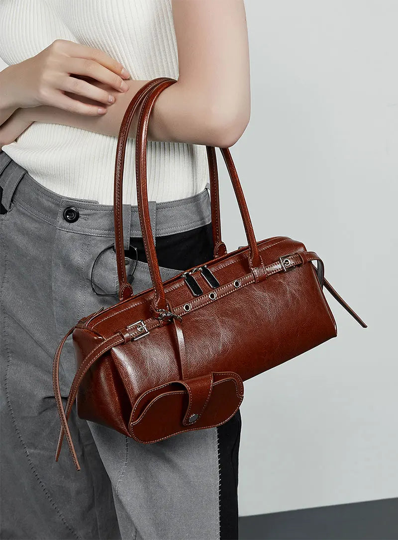 Brown leather handbag held by a person wearing gray pants against a light background