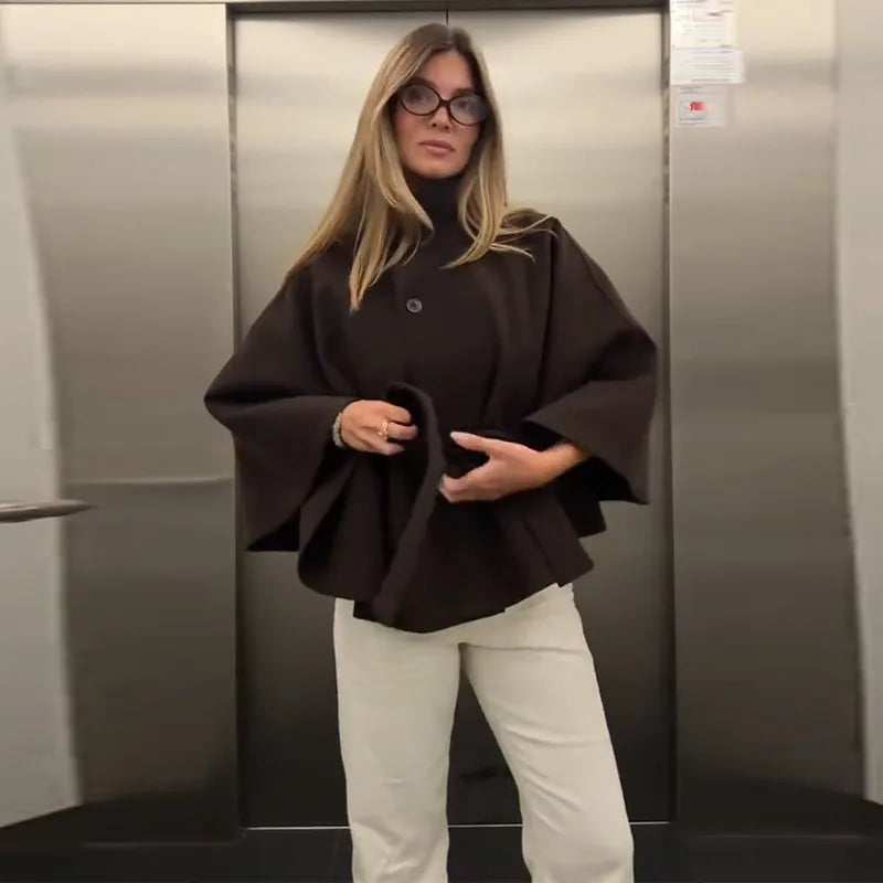Woman wearing a black cape and white pants standing in an elevator.
