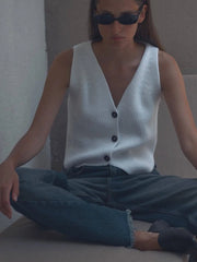  A woman wearing a stylish knitted vest over a white button-down shirt and jeans. Golden Atelier  4