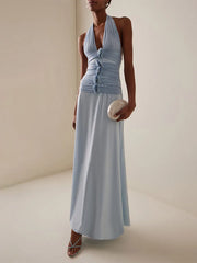 Woman wearing a light blue halter neck dress holding a clutch against a neutral background
