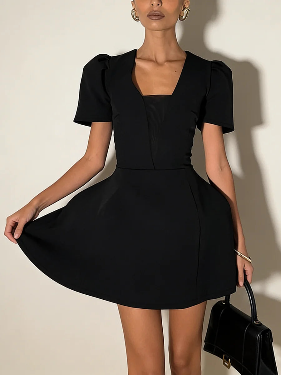 Woman wearing a black dress holding a black handbag against a neutral background