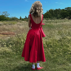 Person wearing a red dress standing in a grassy field with trees in the background
