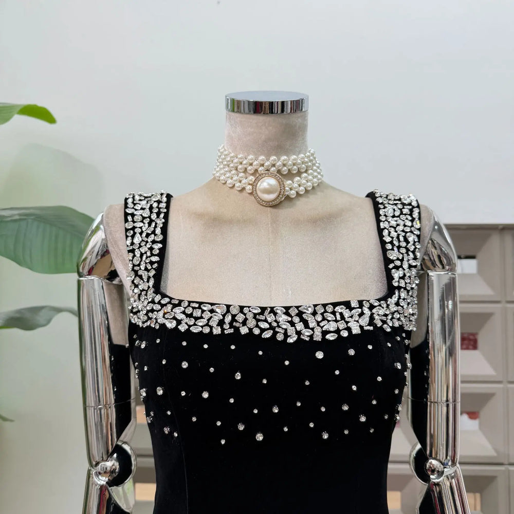 Mannequin wearing a black dress with white embellishments and pearl necklace.