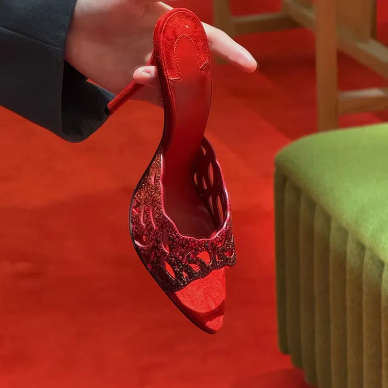A person holding a red suede stiletto slide with crystal cutout