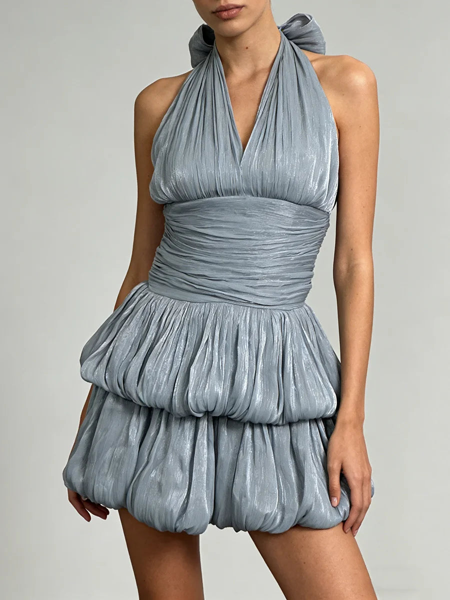Woman wearing a blue halter dress with ruched details on a grey background