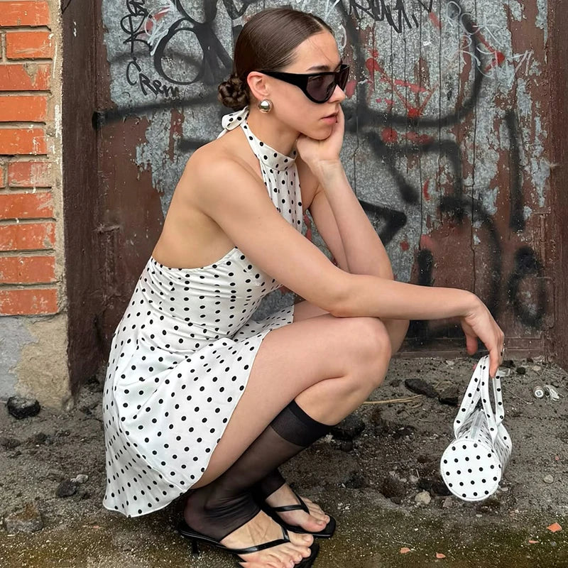 Woman in a polka dot dress and sunglasses sitting against a graffiti-covered wall.