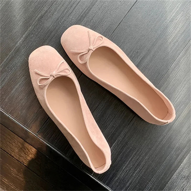 Pink suede ballet flats with bowknot on dark wooden floor