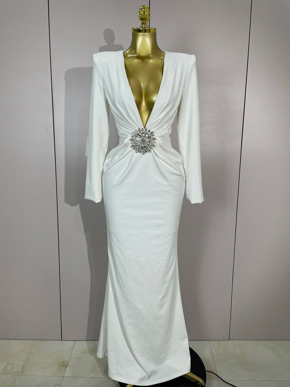 White evening gown with a silver brooch on a mannequin against a plain background