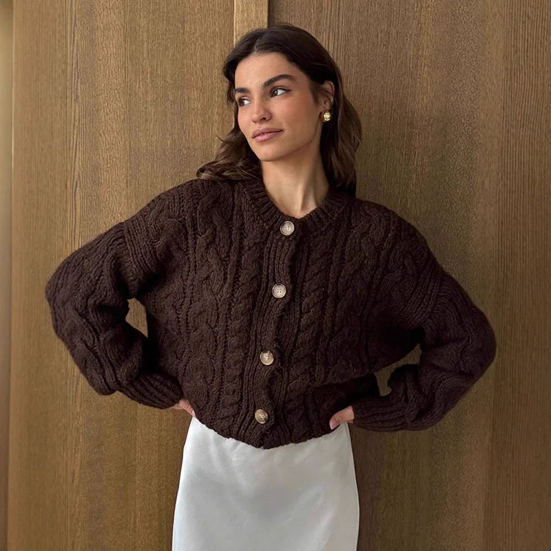 Woman wearing a brown cable knit cardigan against a wooden paneled wall.