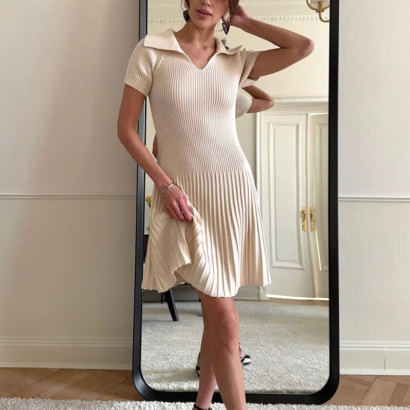 Woman wearing a beige dress standing in front of a full-length mirror.